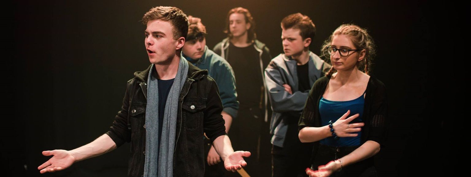 Acting student with arms spread, and other students in background as part of a play