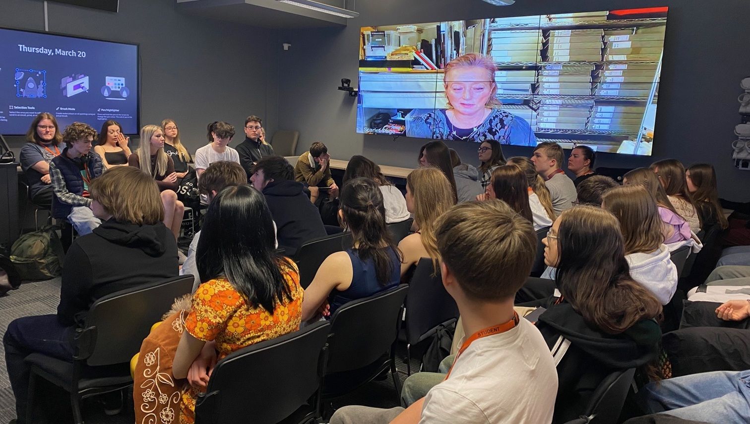 Group of students in a classroom with person on TV Screens