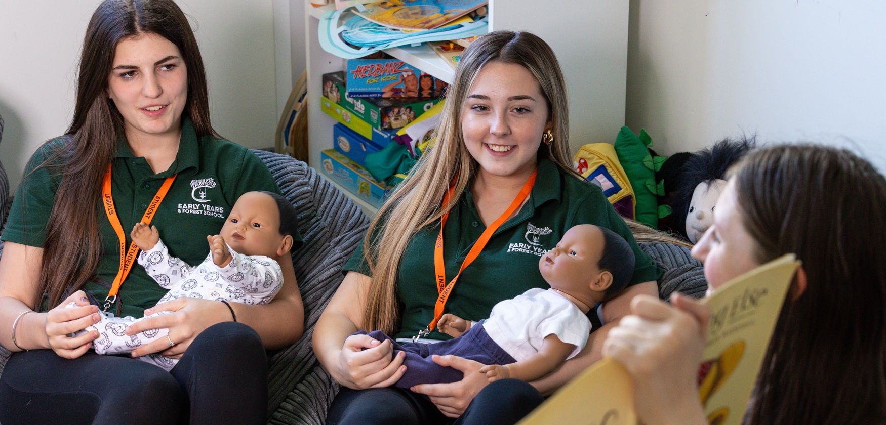 Three students in classroom, two holding baby dolls