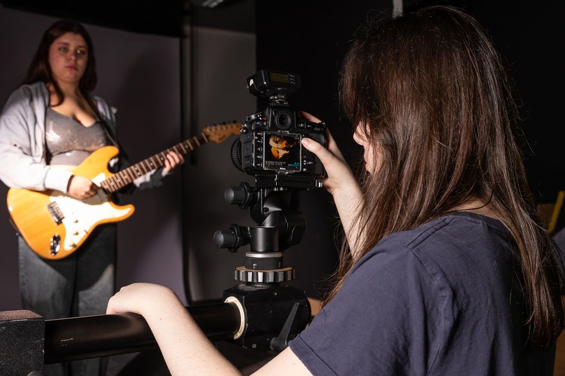 Lady behind camera taking photo of person with guitar