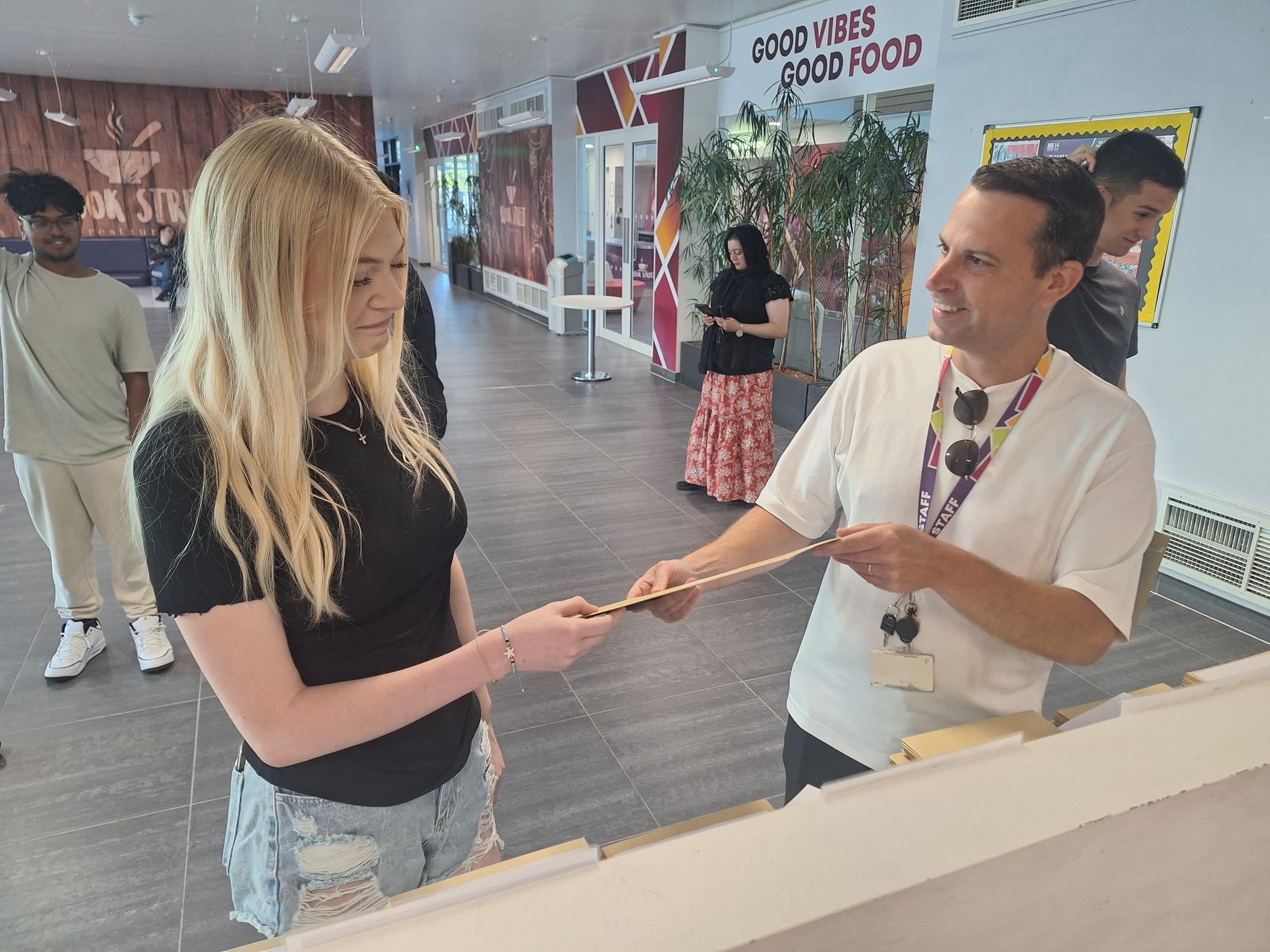 Student being handed an envelope by college staff member