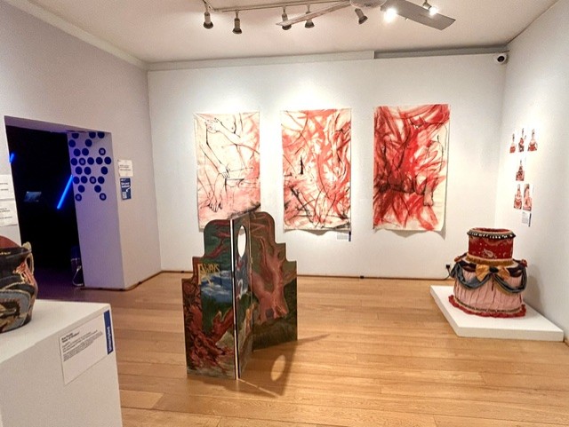 A room in an art gallery with art displayed on walls and floor